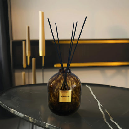 The Greenitial handcrafted reed diffuser with a brown and black leopard-speckled glass vessel placed on a marble desktop in a modern interior setting, demonstrating its use in home decor.