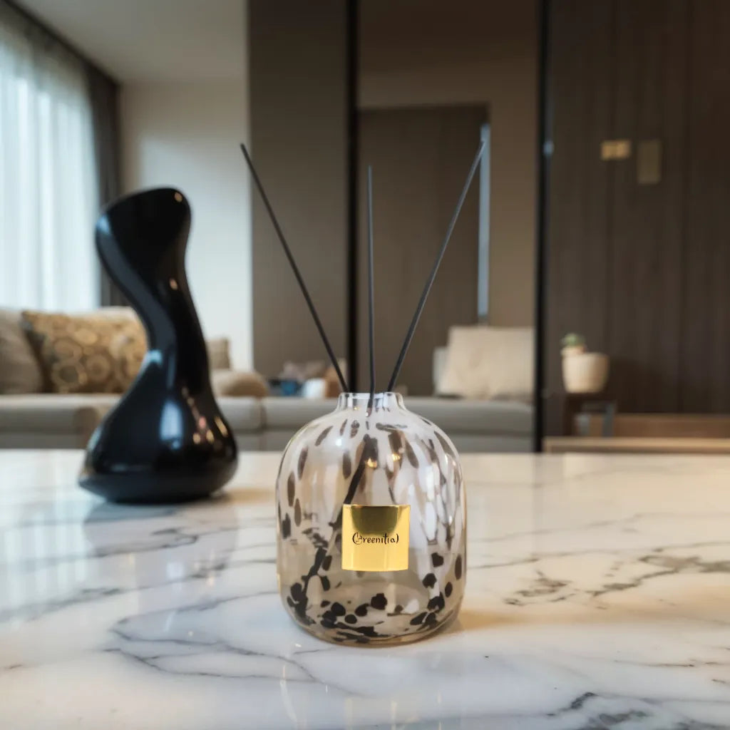 Greenitial handcrafted reed diffuser vessel with a white and black leopard-speckled glass design, standing on a marble tabletop.