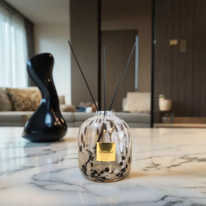 Greenitial handcrafted reed diffuser vessel with a white and black leopard-speckled glass design, standing on a marble tabletop.