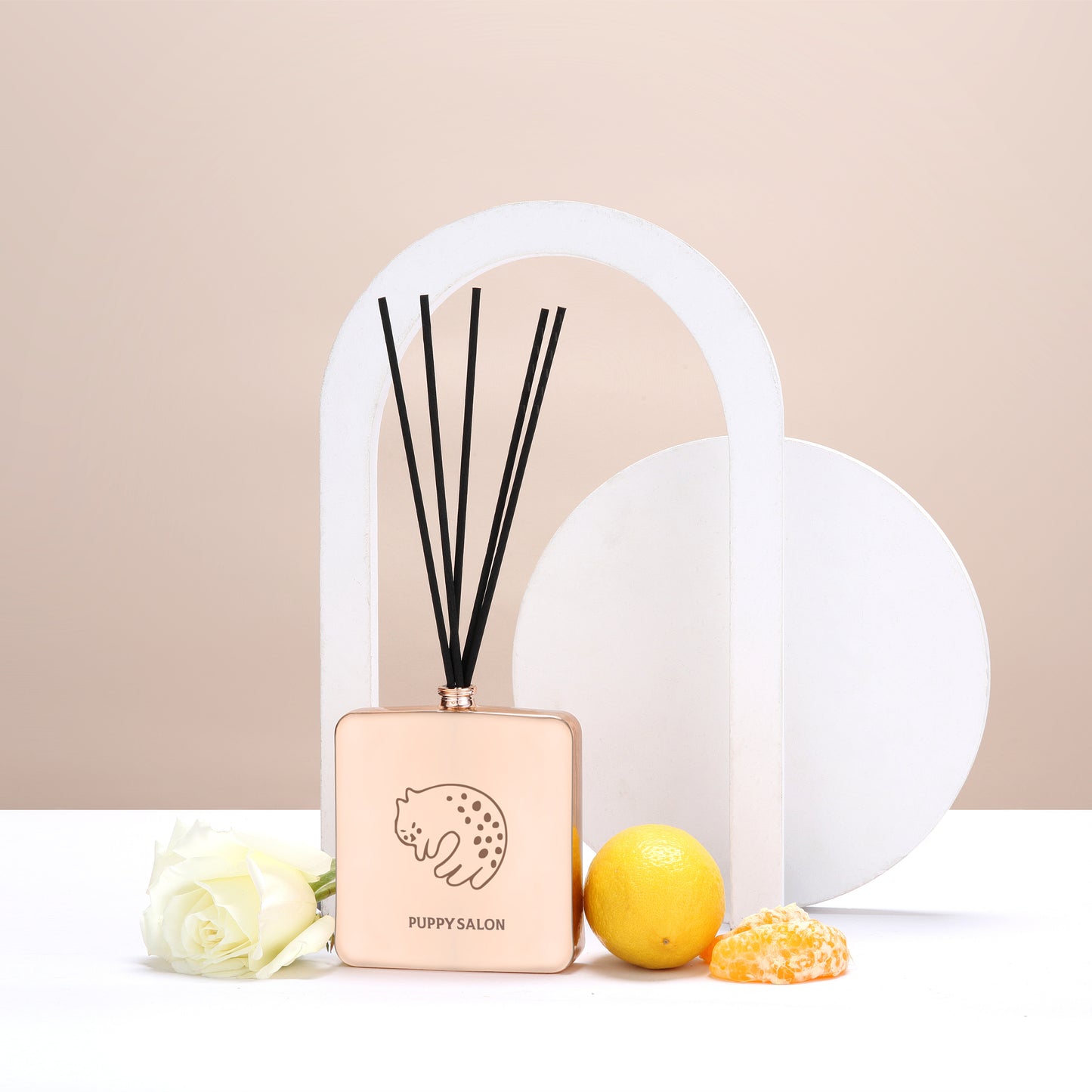 Lifestyle image of the Puppy Salon cat-inspired reed diffuser surrounded by citrus fruits and roses, representing its fresh, floral-citrus fragrance notes.