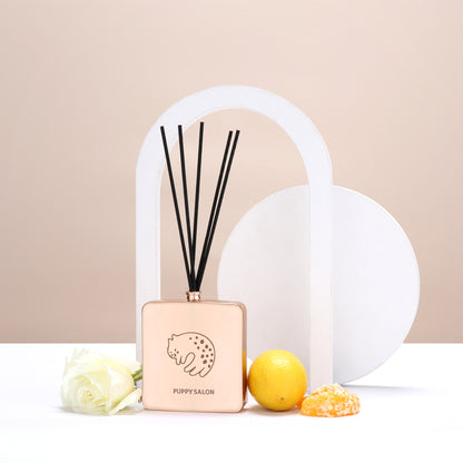 Lifestyle image of the Puppy Salon cat-inspired reed diffuser surrounded by citrus fruits and roses, representing its fresh, floral-citrus fragrance notes.
