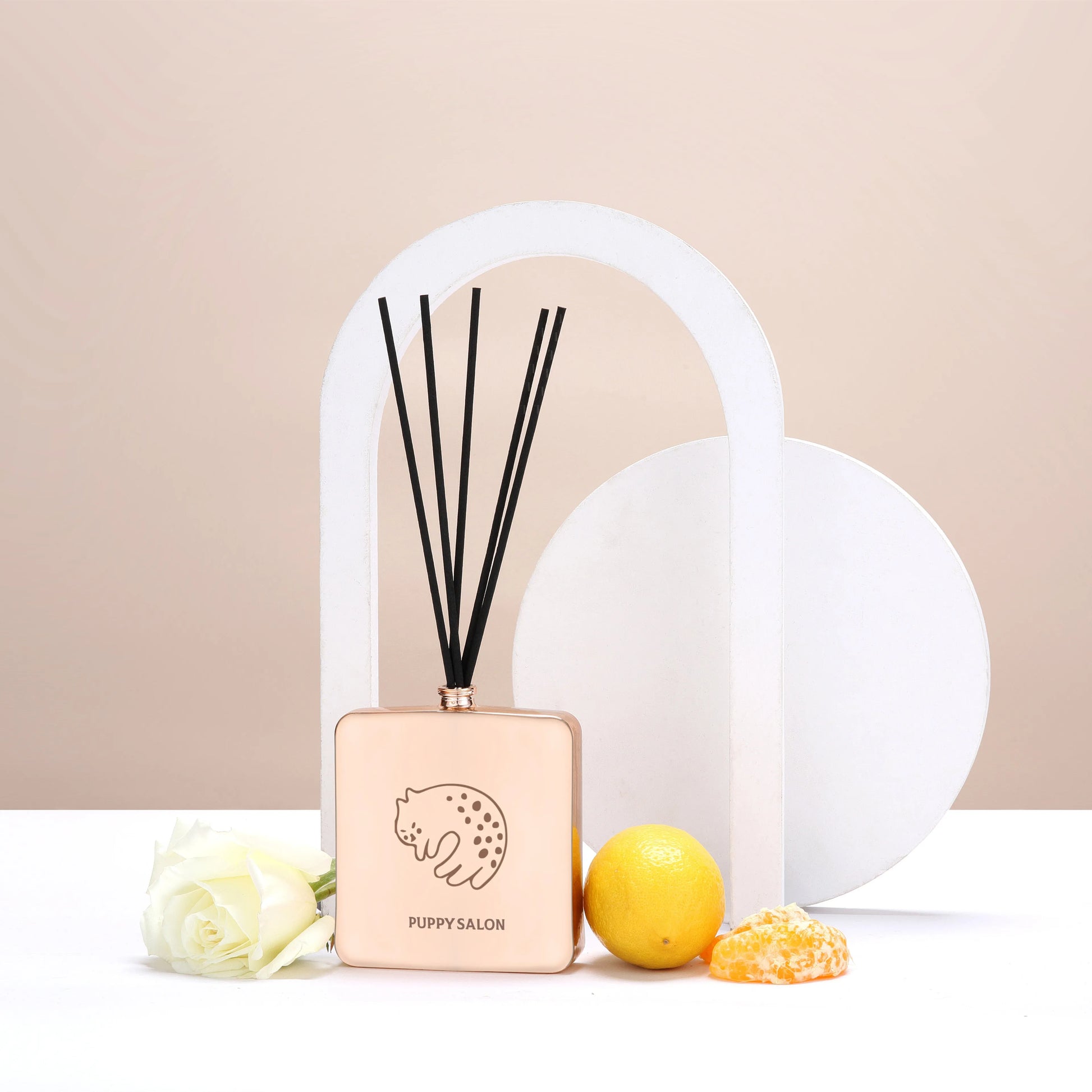 Lifestyle image of the Puppy Salon cat-inspired reed diffuser surrounded by citrus fruits and roses, representing its fresh, floral-citrus fragrance notes.