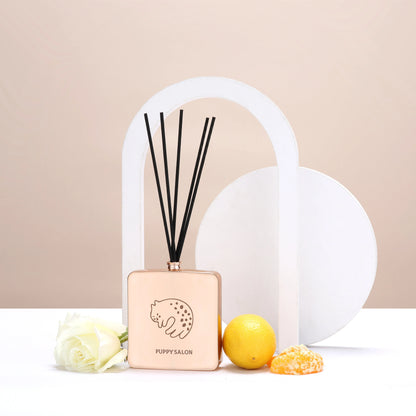 Lifestyle image of the Puppy Salon cat-inspired reed diffuser surrounded by citrus fruits and roses, representing its fresh, floral-citrus fragrance notes.