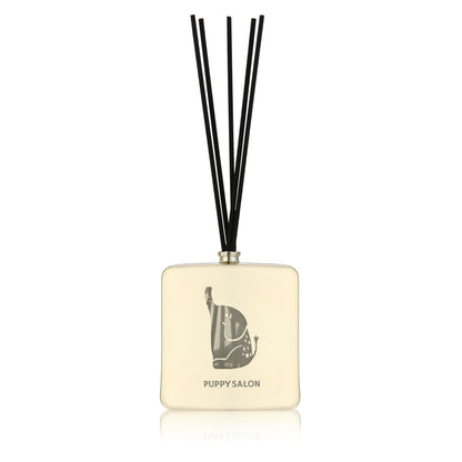 Isolated view of the Puppy Salon reed diffuser. The champagne gold glass bottle features intricate elephant cut-out designs, creating a play of light and liquid.